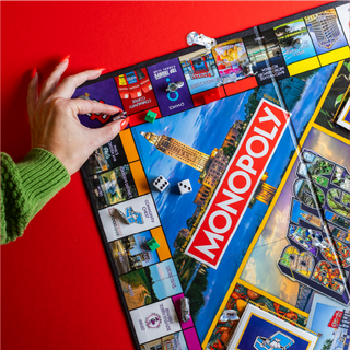 A hand placing a game piece on the Monopoly Baton Rouge Edition game board.