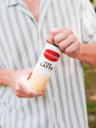 A person opening a Community Coffee Caramel Dream Iced Latte can.