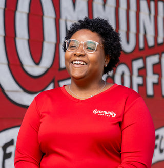 A smiling woman wearing a red Community Coffee long-sleeve shirt.