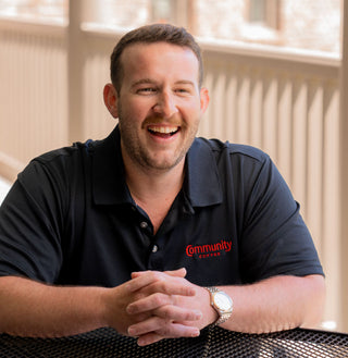 A laughing man wearing a black Community Coffee polo shirt.