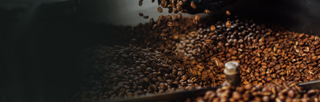 A handful of roasted coffee beans, rich dark-brown in color, fall into a pile of other roasted coffee beans.