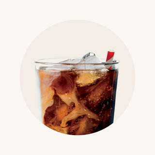 A close-up of a glass of iced coffee, swirled with cream and dotted with condensation, with a straw sticking out.