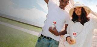 Two young people stand in a field holding Community Coffee Iced Latte cans.
