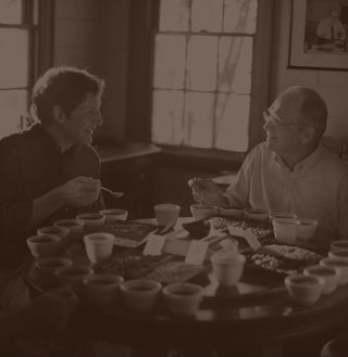 Fourth-generation Community Coffee owner Matt Saurage and third-generation owner Norman Saurage the Third share a smile while testing coffees around a table.