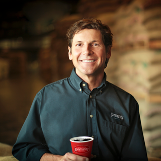 Fourth-generation Community Coffee owner Matt Saurage smiles while holding a cup of coffee.
