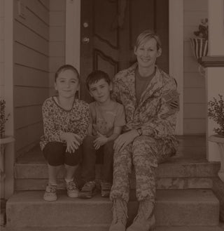 A woman dressed in military attire sits on a front porch next to two children.