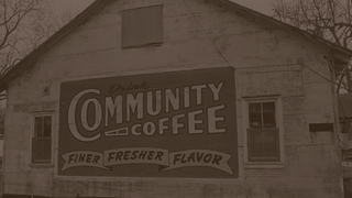 A sign reading DRINK COMMUNITY COFFEE, FINER FRESHER FLAVOR on an old building, shown in sepia tone.