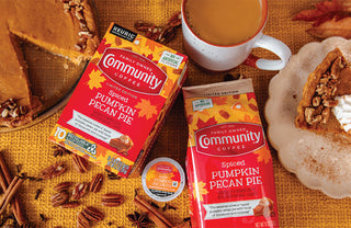 Packages of Community Coffee Spiced Pumpkin Pecan Pie lie on a table, next to a cup of rich brown coffee and slices of pecan pie.