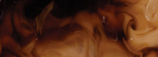 Cream swirls through rich, dark-brown coffee.