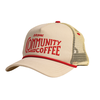 A cream-colored trucker hat reading DRINK COMMUNITY COFFEE in red text.